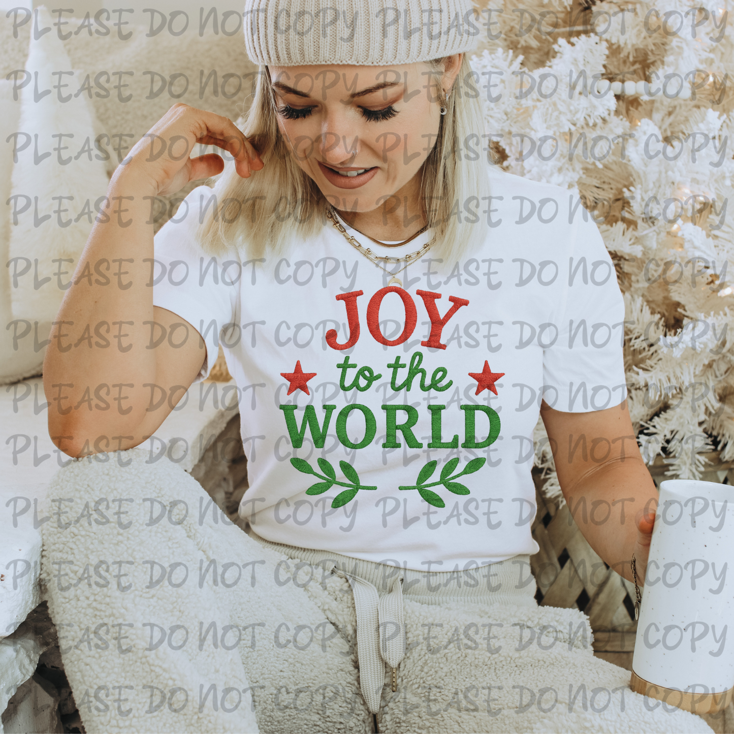 Woman wearing a white t-shirt with 'Joy to the World' text, sitting on a couch.