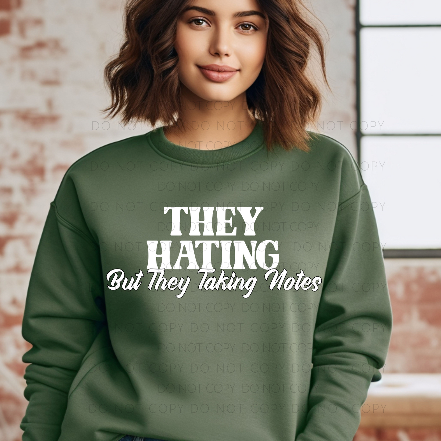 A person wearing a green crew neck t-shirt with the text 'THEY HATING But they taking Notes' printed on the front.