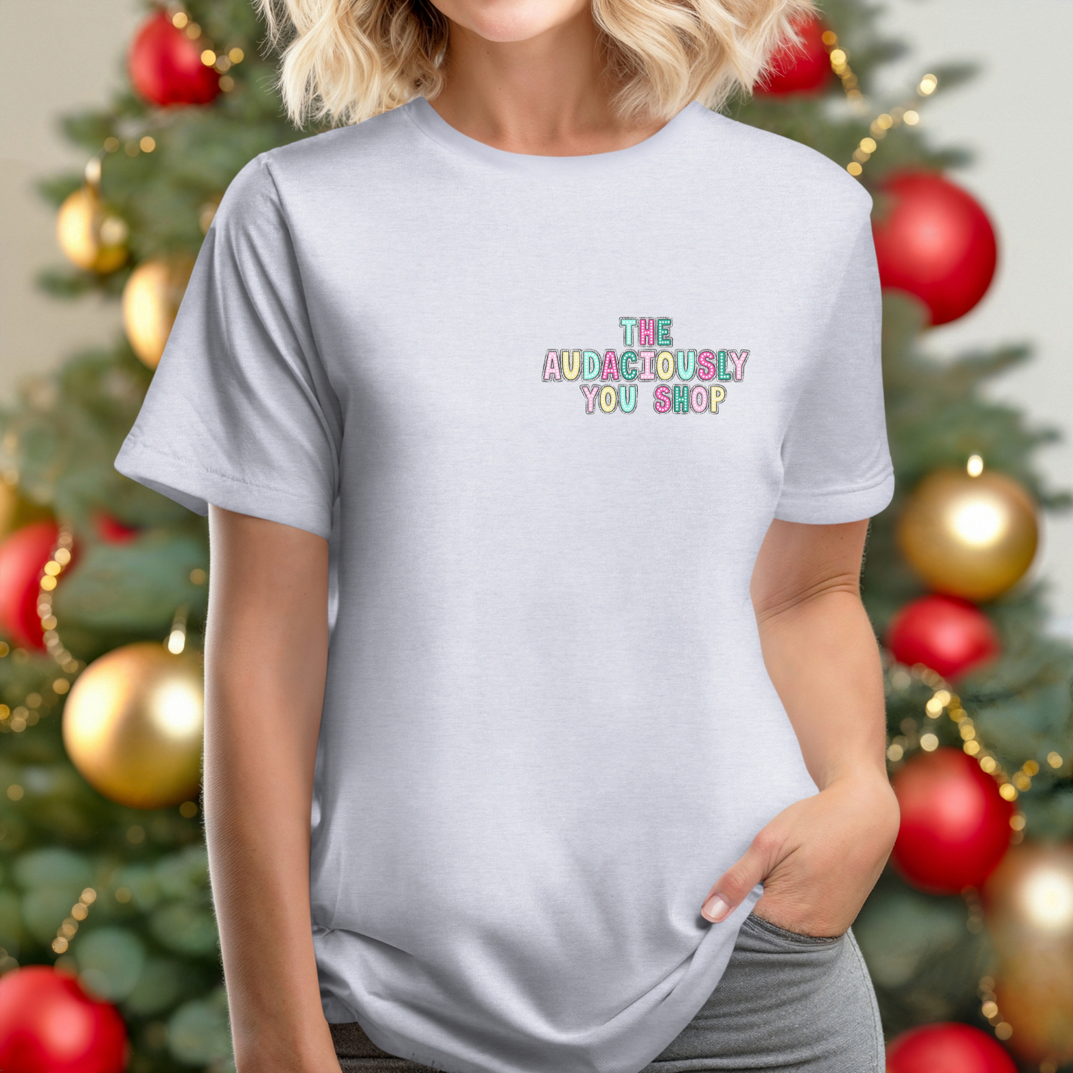 Person wearing a light gray t-shirt with colorful text in front of a decorated Christmas tree.