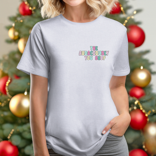 Person wearing a light gray t-shirt with colorful text in front of a decorated Christmas tree.