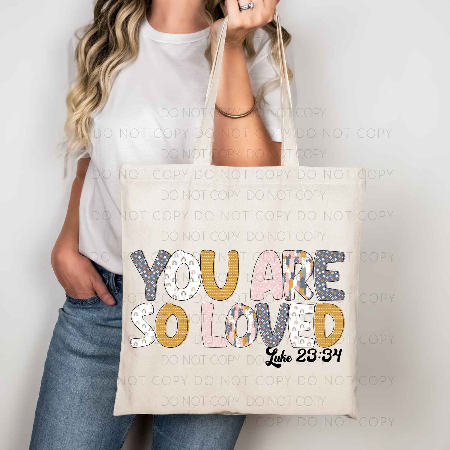 A person holding a beige cotton tote bag with the text 'YOU ARE SO LOVED' printed in various colors.