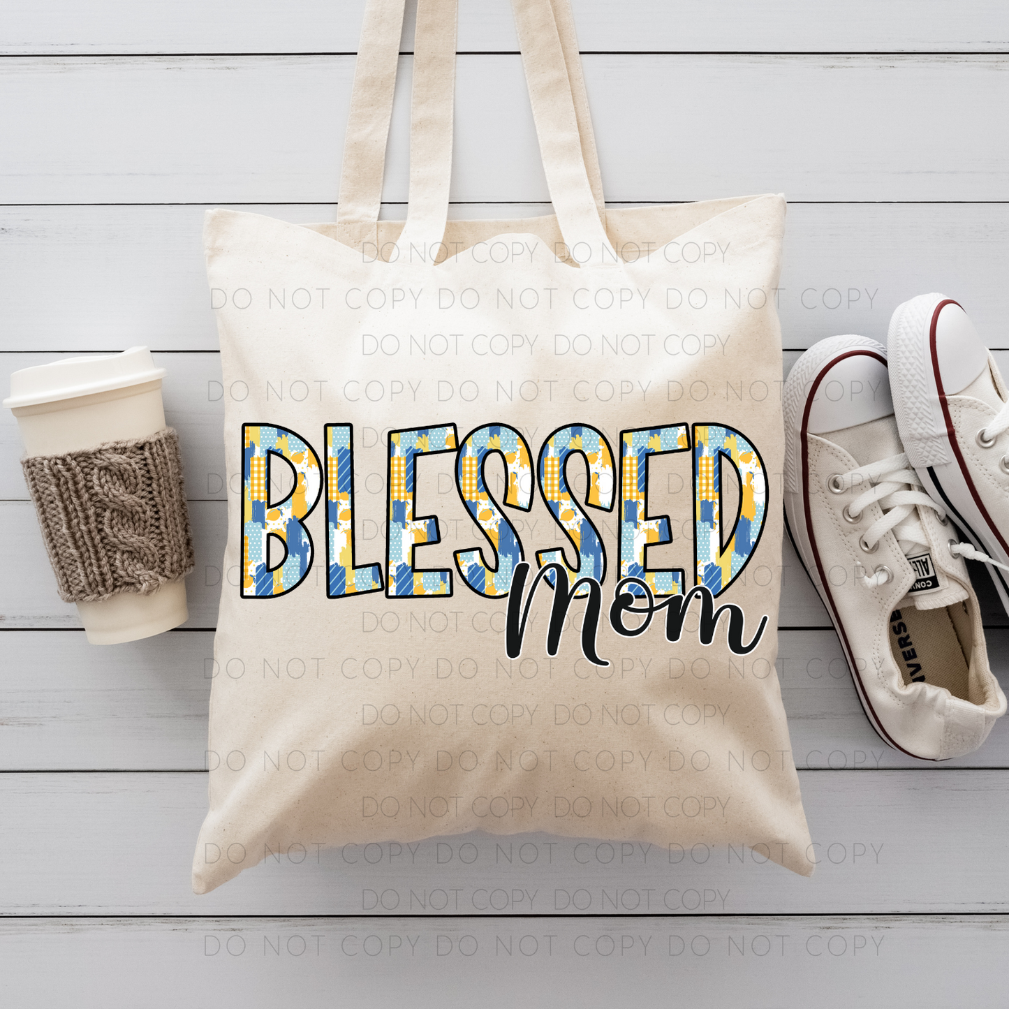 A beige cotton tote bag with 'Blessed Mom' printed in blue and yellow dual-sided DTF print, accompanied by a pair of white sneakers and a brown knit hat on a wooden surface.