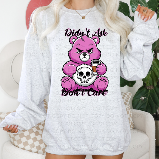 A graphic unisex t-shirt with a design featuring a pink bear holding a skull and the text 'Didn't Ask Don't Care'.
