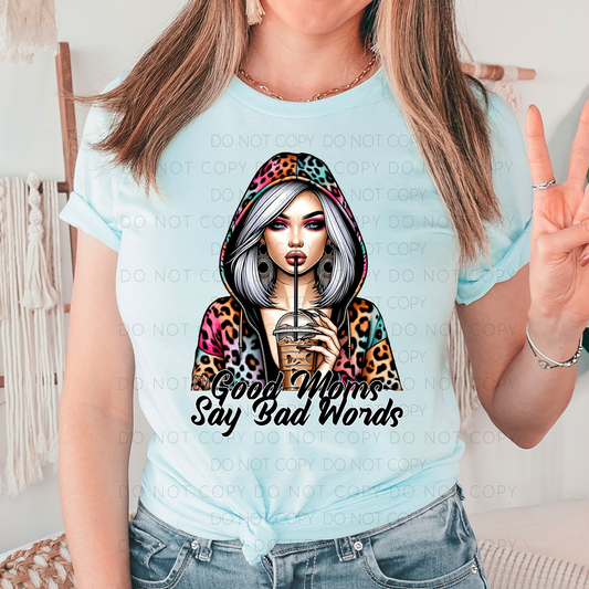 A person wearing a blue unisex t-shirt with a graphic design of a woman with a leopard print hat and the text 'Good Moms Say Bad Words'.