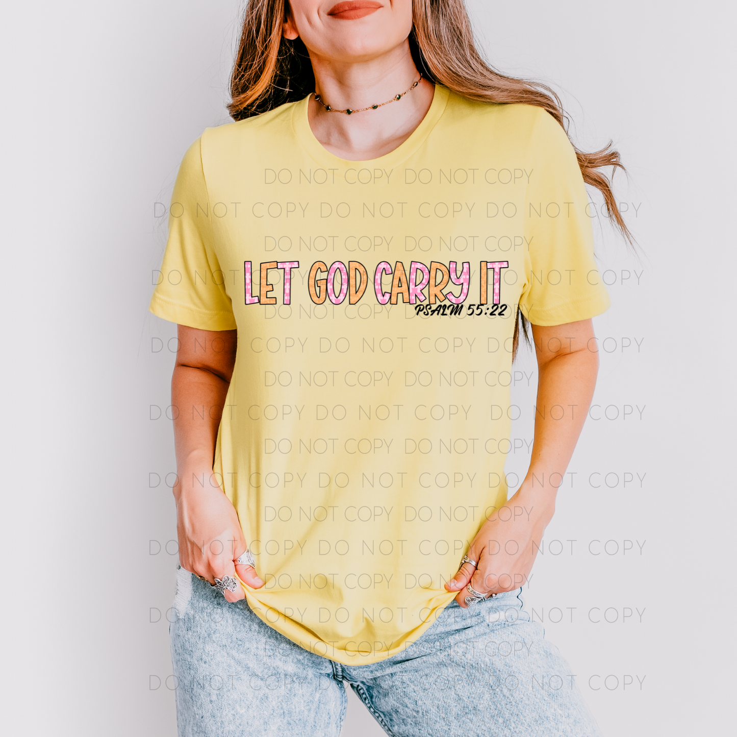 A person wearing a yellow unisex t-shirt with the text 'LET GOD CARRY IT' printed on the front.