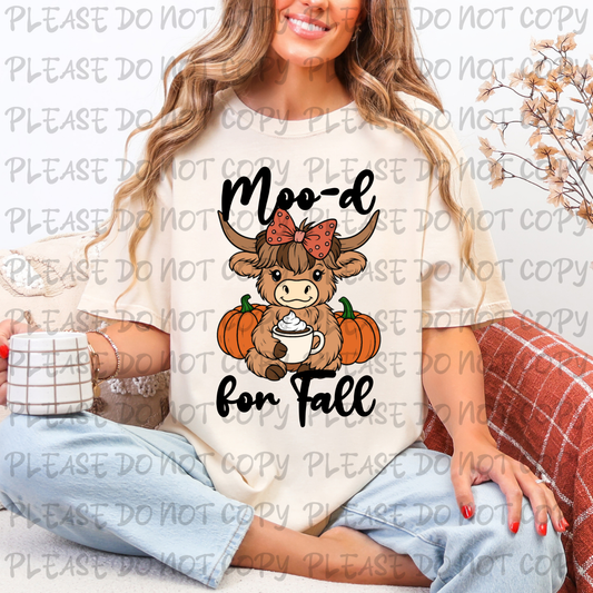 Woman wearing a shirt with a cow graphic and 'Moo-d for Fall' text, sitting on a couch.
