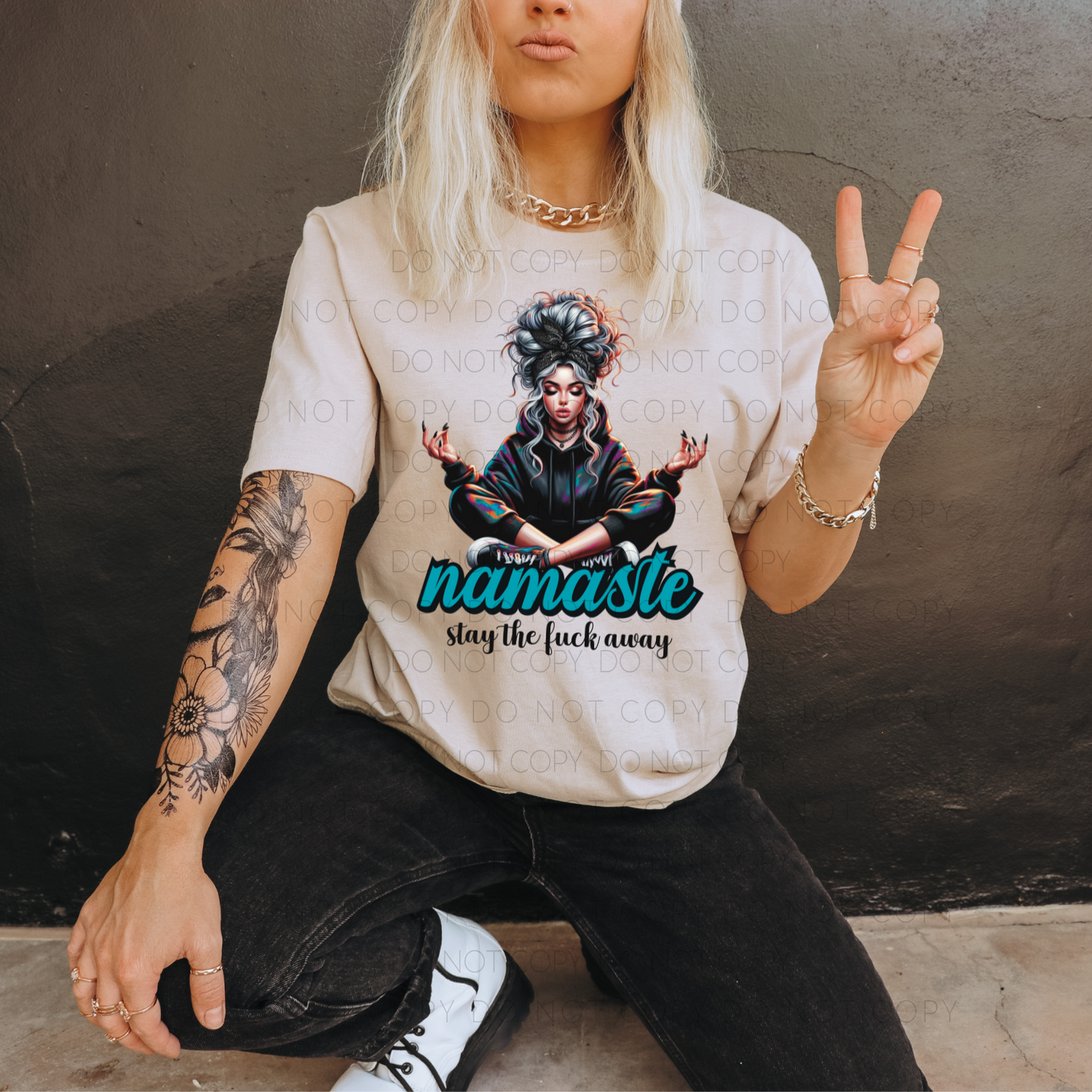 A person posing with a peace sign wearing a beige t-shirt with a graphic design of a character and the text 'namaste' on it.