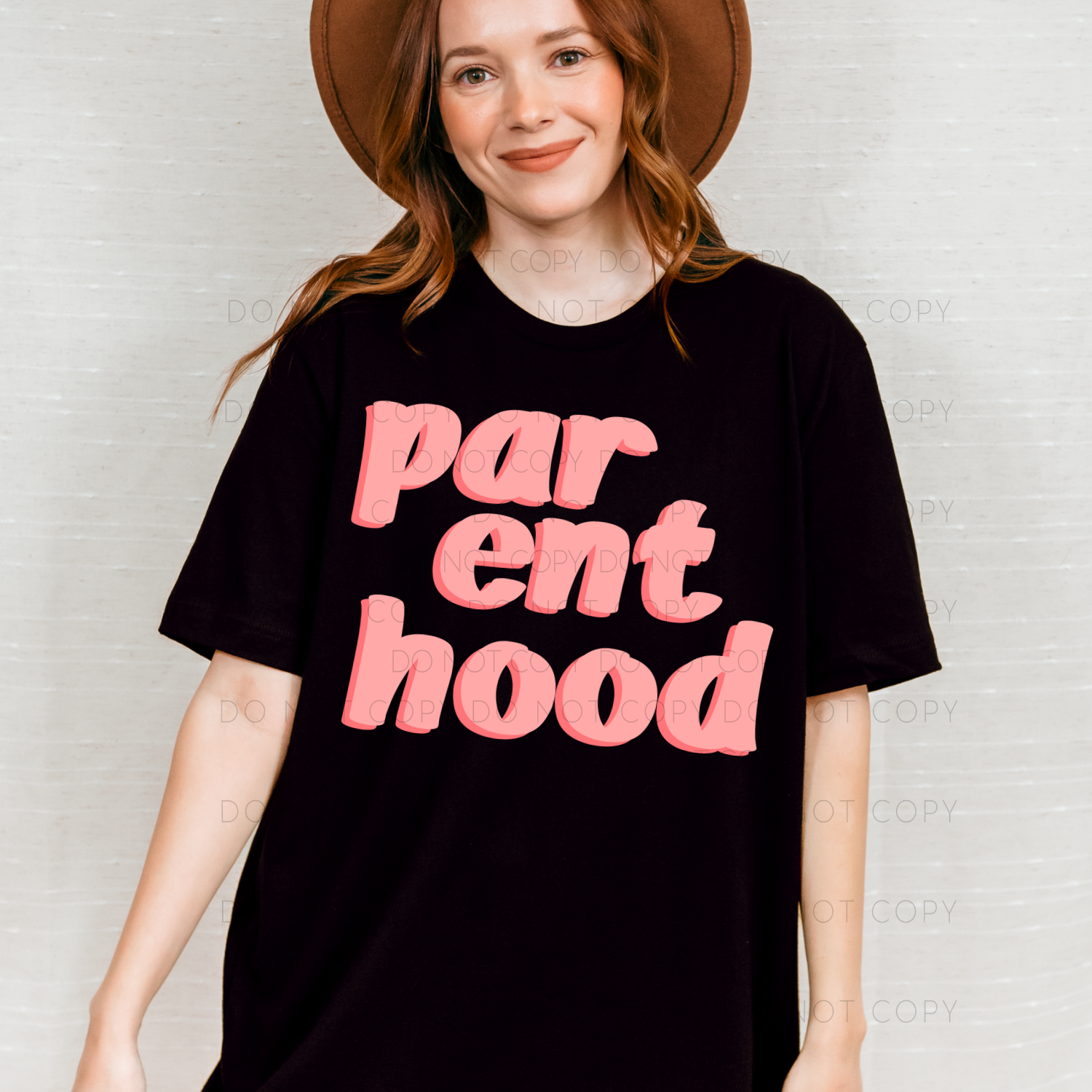 A person wearing a black unisex t-shirt with the text 'parent hood' in pink.