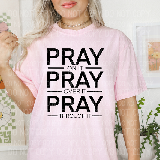 A person wearing a pink unisex t-shirt with the text 'PRAY ON IT, PRAY OVER IT, PRAY THROUGH IT' in black.