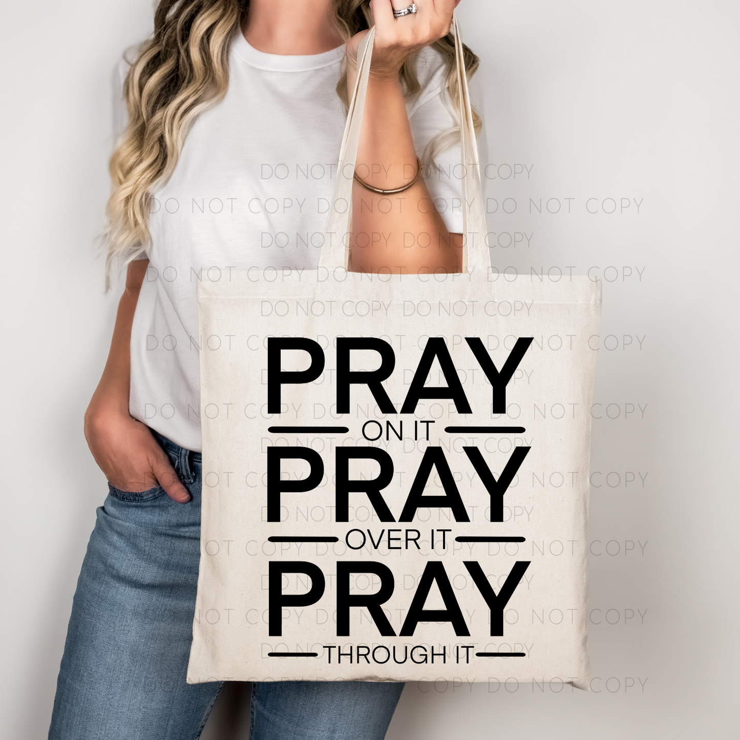 A person holding a cotton tote bag with the text 'PRAY ON IT PRAY OVER IT PRAY THROUGH IT' printed on both sides.