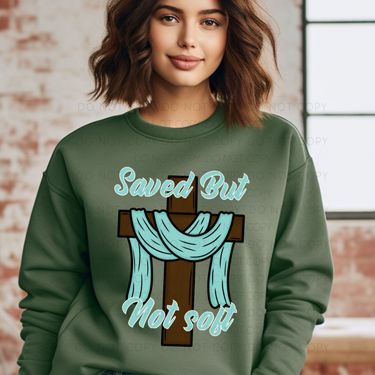 A woman wearing a green crew neck t-shirt with the text 'Saved But Not Soft' on it.
